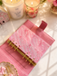 A pink textured leather planner cover with a gold ring binder, shown open on a marble surface with candles and small decorative props around it.