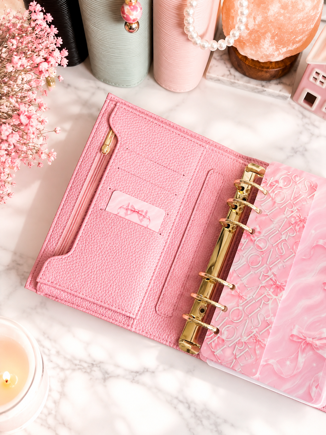 Dreamy Ribbon Cash Breakdown Card displayed inside a pink A6 cash stuffing binder with gold rings on a white marble desk, featuring a feminine pink ribbon design for tracking cash denominations.