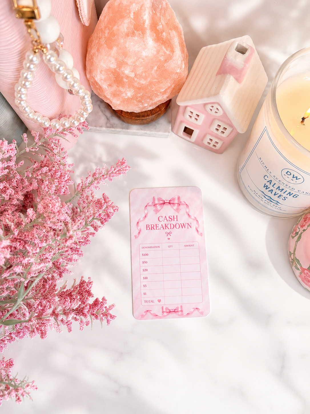 Dreamy Ribbon Cash Breakdown Card displayed inside a pink A6 cash stuffing binder with gold rings on a white marble desk, featuring a feminine pink ribbon design for tracking cash denominations.