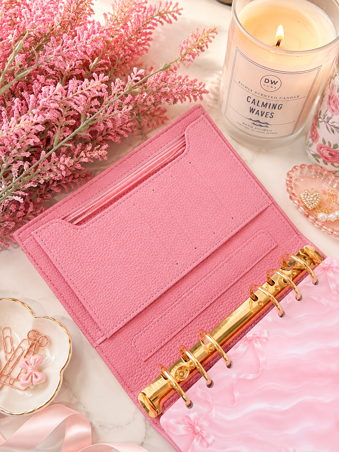 Open pink cash stuffing binder for budgeting with spacious storage, gold binder rings, and elegant feminine desk styling including candles, flowers, and marble accents.