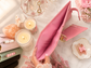 Open pastel pink budgeting binder with gold rings and multiple storage compartments on a bright marble desk surrounded by lit candles, flowers, and pink office accessories.
