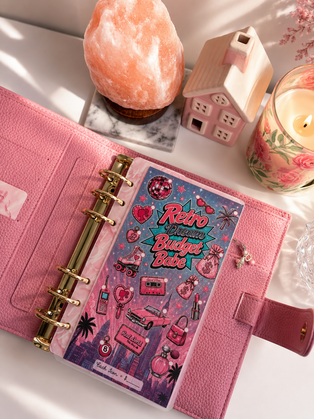 Retro Dream Budget Babe A6 savings challenge dashboard inside a pink cash stuffing binder featuring retro-inspired pink and teal graphics, including a vintage car, roller skates, perfume, lipstick, money bags, and disco ball, styled with a Himalayan salt lamp, floral candle, and cozy feminine desk decor.